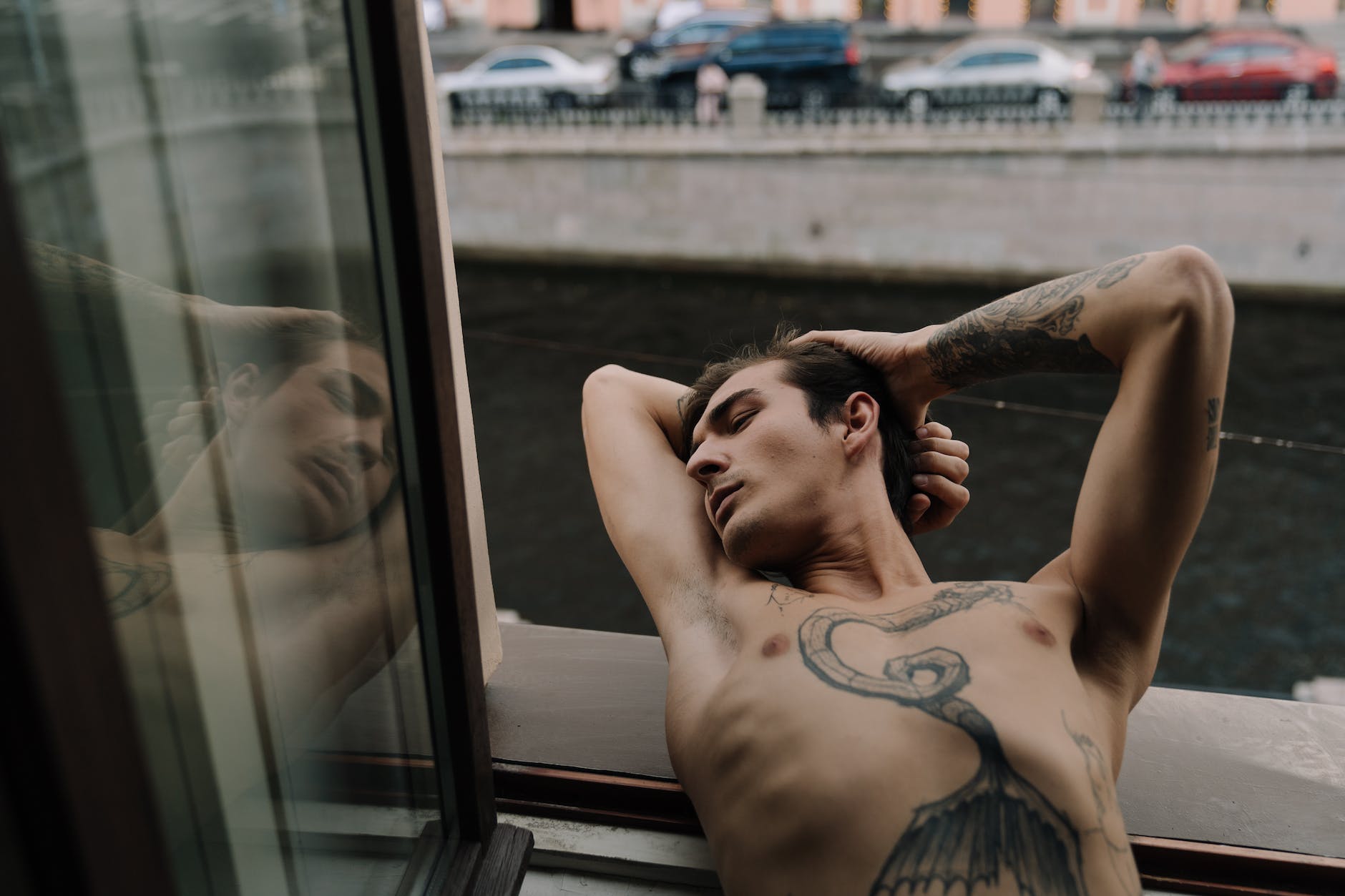 topless man with tattoo lying on window sill